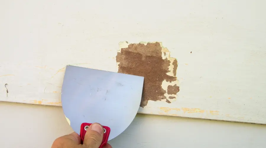 painter preparing exterior surface by scraping and sanding before painting